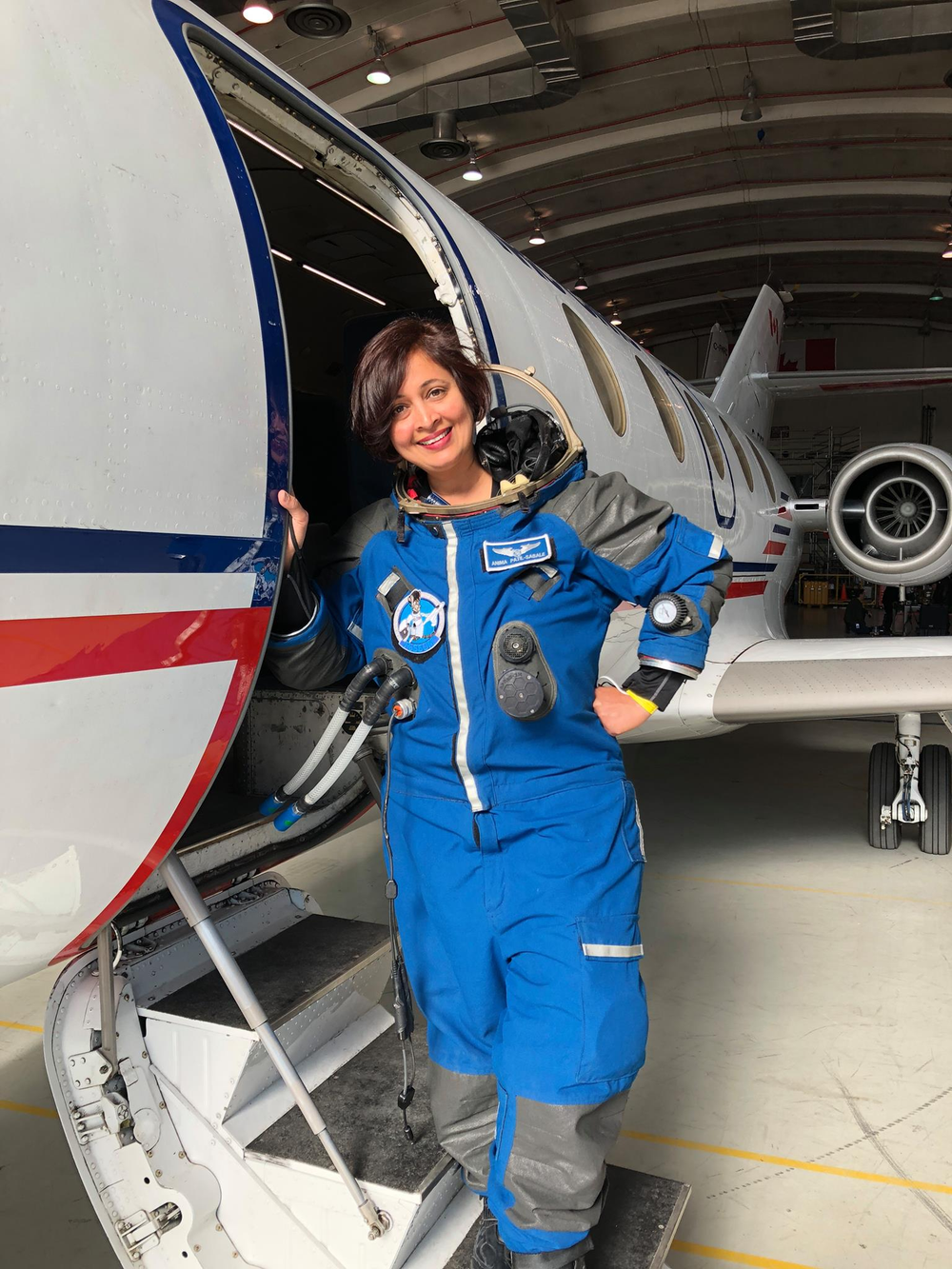 A woman in a spacesuit stands at the doorway to a small jet airplane.