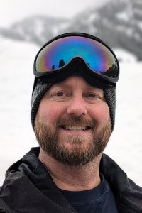 Image of a smiling man with ski goggles on his forehead.