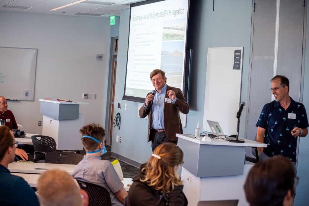 A man with a mic speaks to a room full of people.