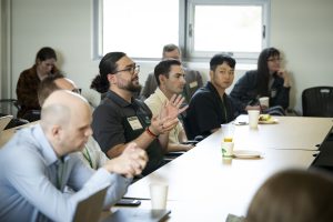 A man gestures as he asks a question at the conference with a room full of attendees around him.