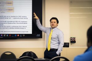 A man gestures as he explains his research at a lecture presentation.