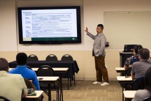 A man gestures as he explains his research at a lecture presentation.