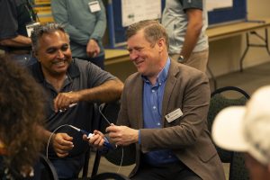 Two men smile as they examine a medical device that looks like a cable with a hand control.