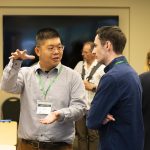 A man gestures as he explains his research at a poster presentation.