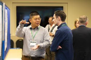A man gestures as he explains his research at a poster presentation.