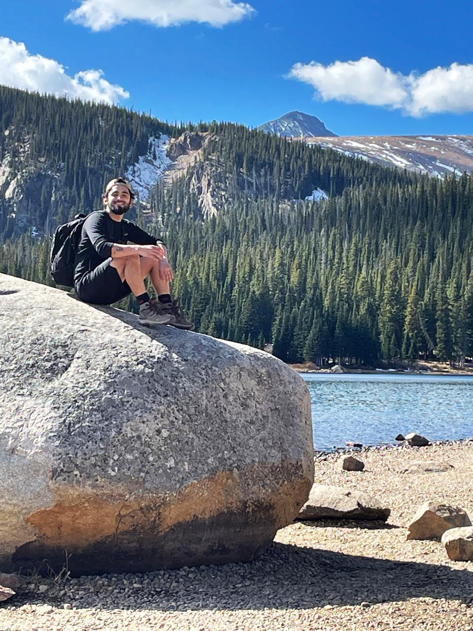 A man sits on a boulder near a mountain lake.