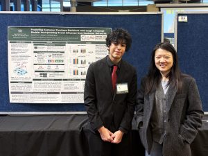 A young man stands with a woman in front of a poster.