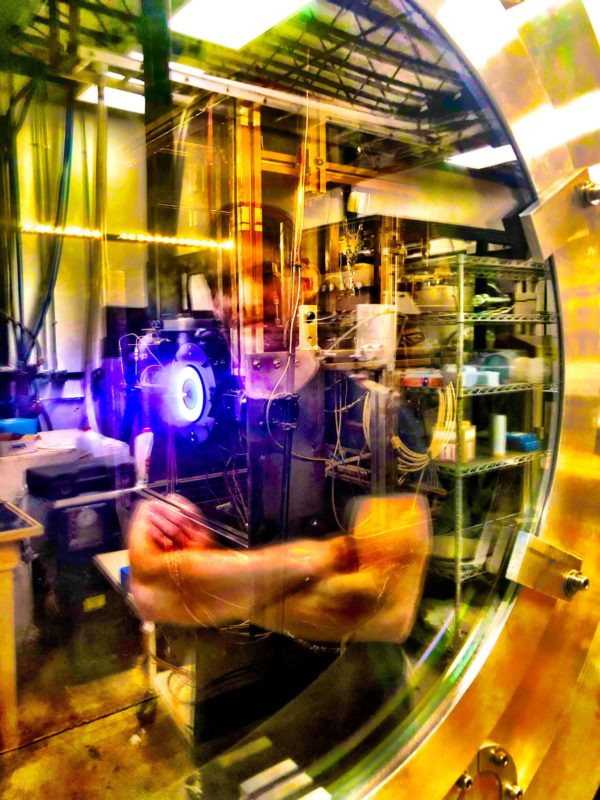 Reflection of graduate student Thomas Andreano as he watches his 2 kW Kr Hall thruster whose light is being transmitted through a window port of a large vacuum chamber at CSU. Photo credit: Professor John Williams