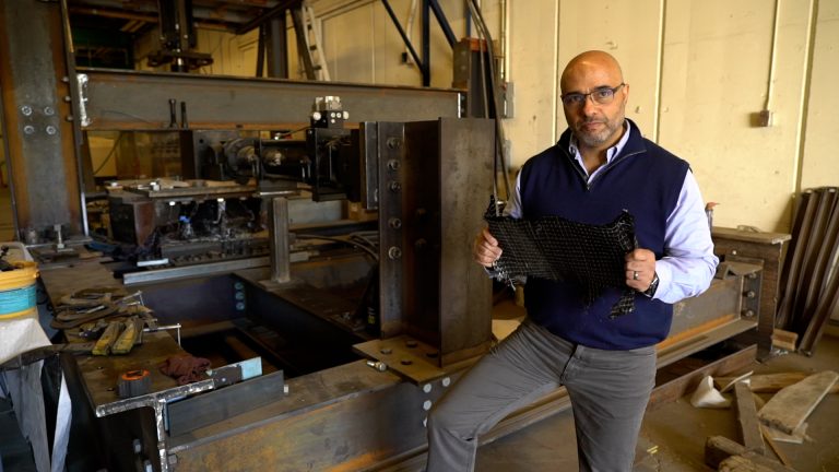 CSU Civil and Environmental Engineering Professor Hussam Mahmoud stands in front of an experiment, holding a piece of metal.