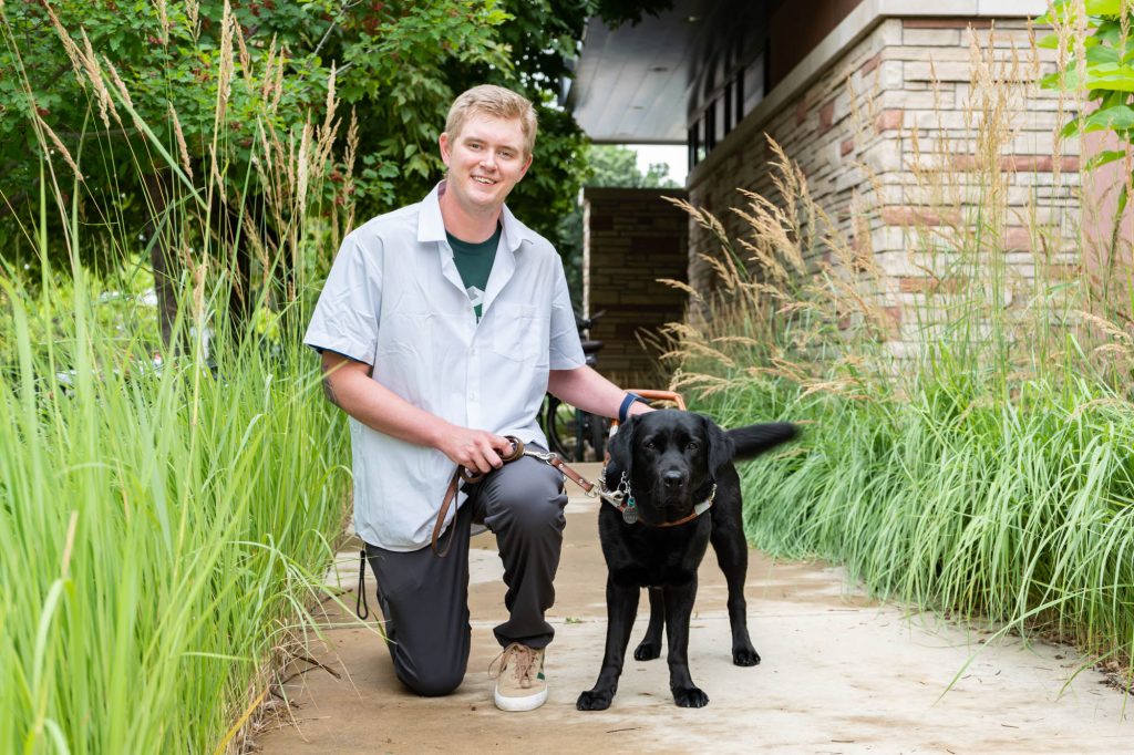 Colorado State University environmental engineering student Robert Lamm and his service canine Fletcher pose in the Atrium of the Suzanne and Walter Scott, Jr. Bioengineering Building, July 26, 2023. Credit: Walter Scott, Jr. College of Engineering.
