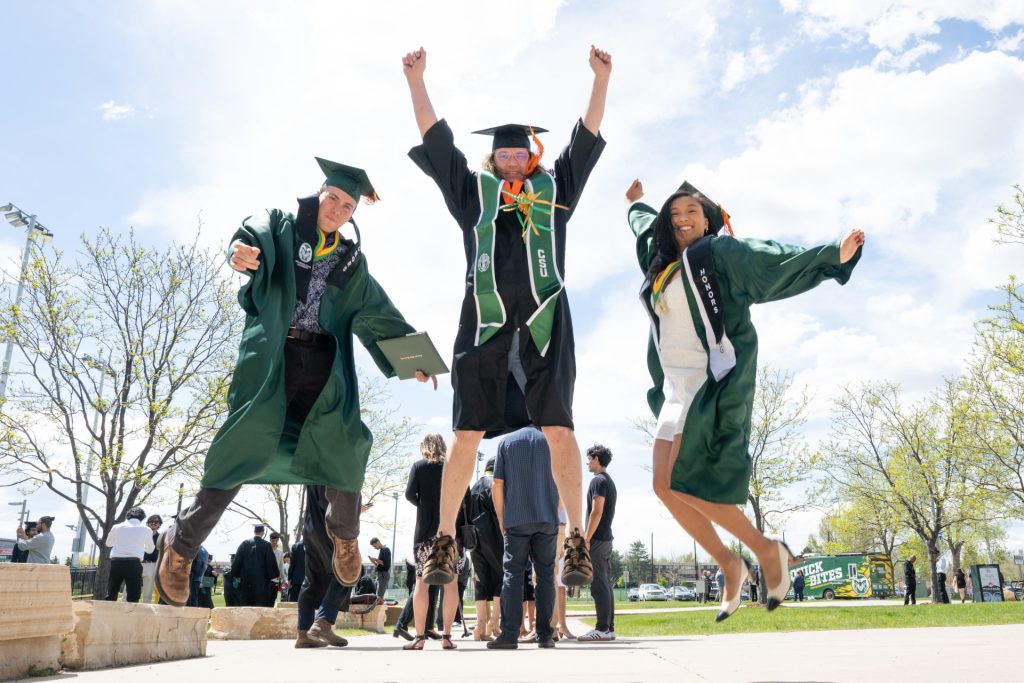 Three people in graduation regalia celebrates by jumping up..