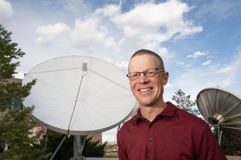 Phil Klotzbach, senior research scientist for the Department of Atmospheric Science in the Walter Scott, Jr. College of Engineering, stands in front of a satellite dish.